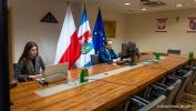 Przy stole prezydialnym siedzą kobieta i mężczyzna. W tle flagi: województwa podkarpackiego, polska oraz unijna