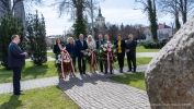 Grupa ludzi z kwaitami stoi przed pomniekiem rocznicy chrztu Polski 