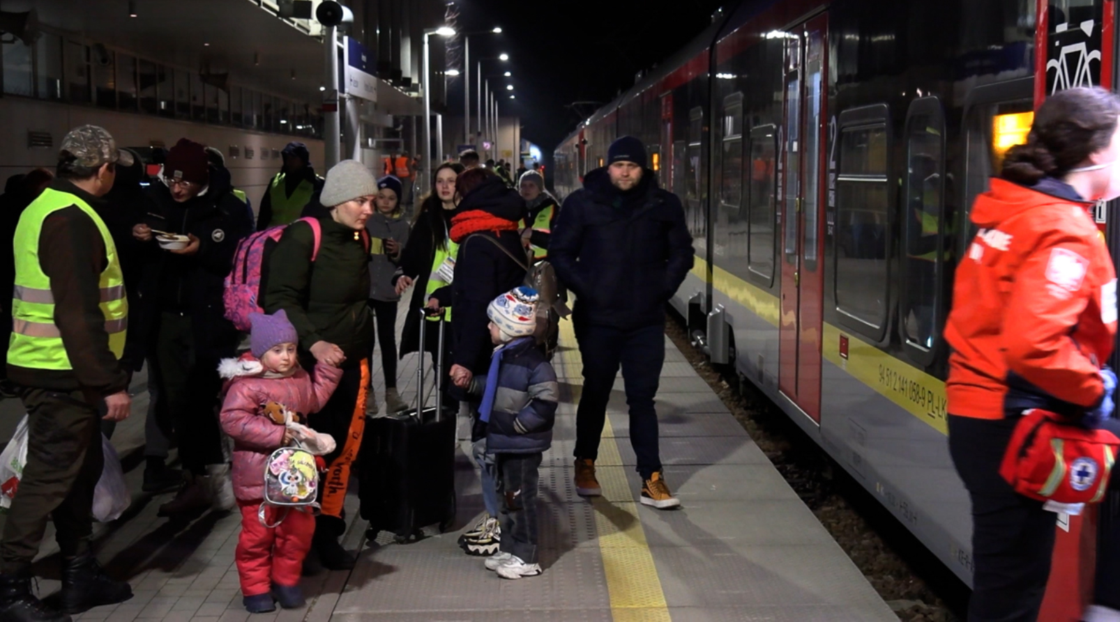 Ludzie czekający na peronie aby wejść do pociągu. Na pierwszym planie matka z małymi dziećmi.