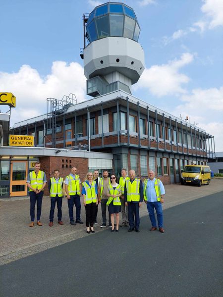 Przedstawiciele Województwa Podkarpackiego z wizytą na lotnisku w Groningen - Airport Eelde.  W tle wieża kontroli lotów. 
